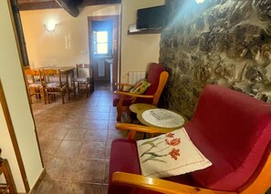 A cozy living area with a red sofa, wooden chairs, and a small round table. A stone wall adds texture to the space.