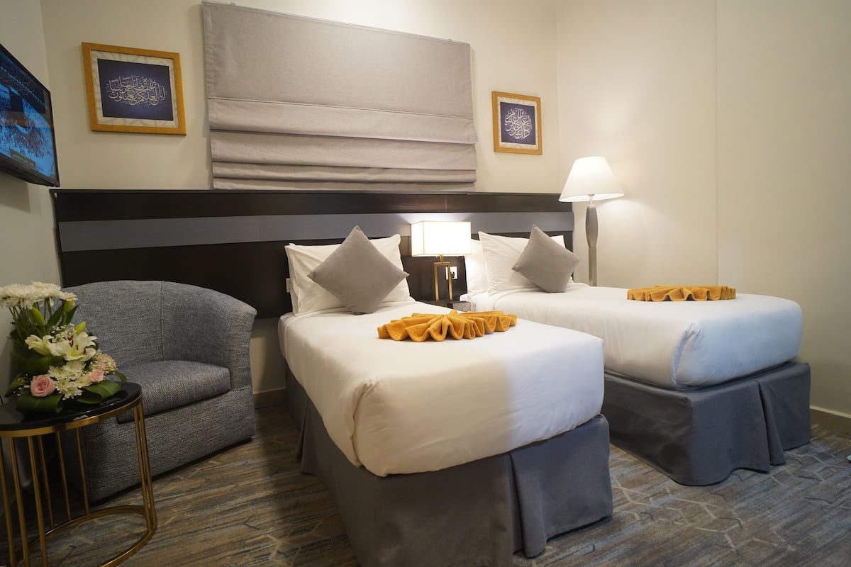 A hotel room with two beds, a sofa, a small table with flowers, and a wall-mounted TV.