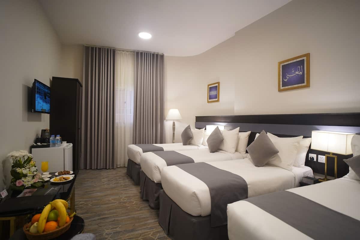 A hotel room with two beds, a desk with a television, a lamp, and a fruit basket.