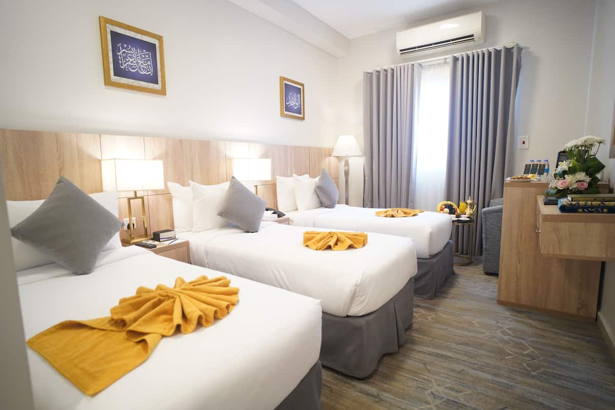 A hotel room with two beds, a desk, a chair, and a small table with a vase of flowers.