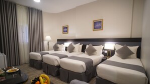 A hotel room with four beds, a dining table, and a fruit basket. - Emaar Andalusia (Makkah)