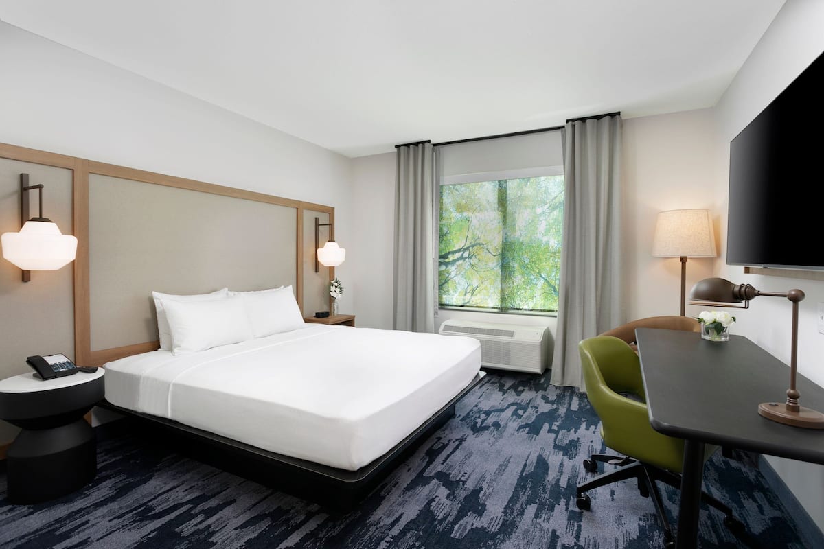A hotel room with a large bed, a desk, a chair, a TV, a phone, and a window with curtains.