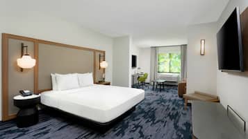 Een hotelkamer met een groot bed, nachtkastjes, een bureau, een stoel, een televisie en een raam met uitzicht op groen.