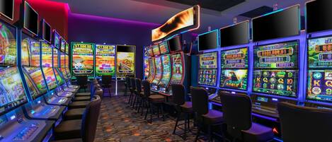 A row of slot machines in a casino with a patterned carpet and chairs.