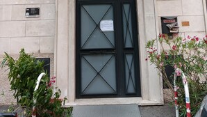 Un bâtiment doté d’une entrée encadrée de noir, d’un balcon avec des garde-corps en métal et d’une enseigne indiquant un espace réservé aux avis publics.