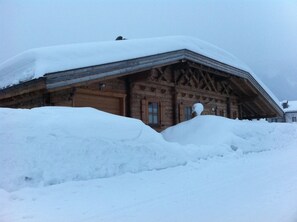 Un chalet en bois, doté d’un toit en pente recouvert de neige, entouré de congères.