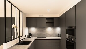 A modern kitchen with dark cabinetry, a built-in oven, and a coffee maker.