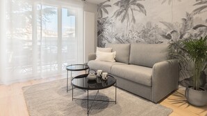 A modern living room with a grey sofa, a round black coffee table, and a large window with sheer curtains.