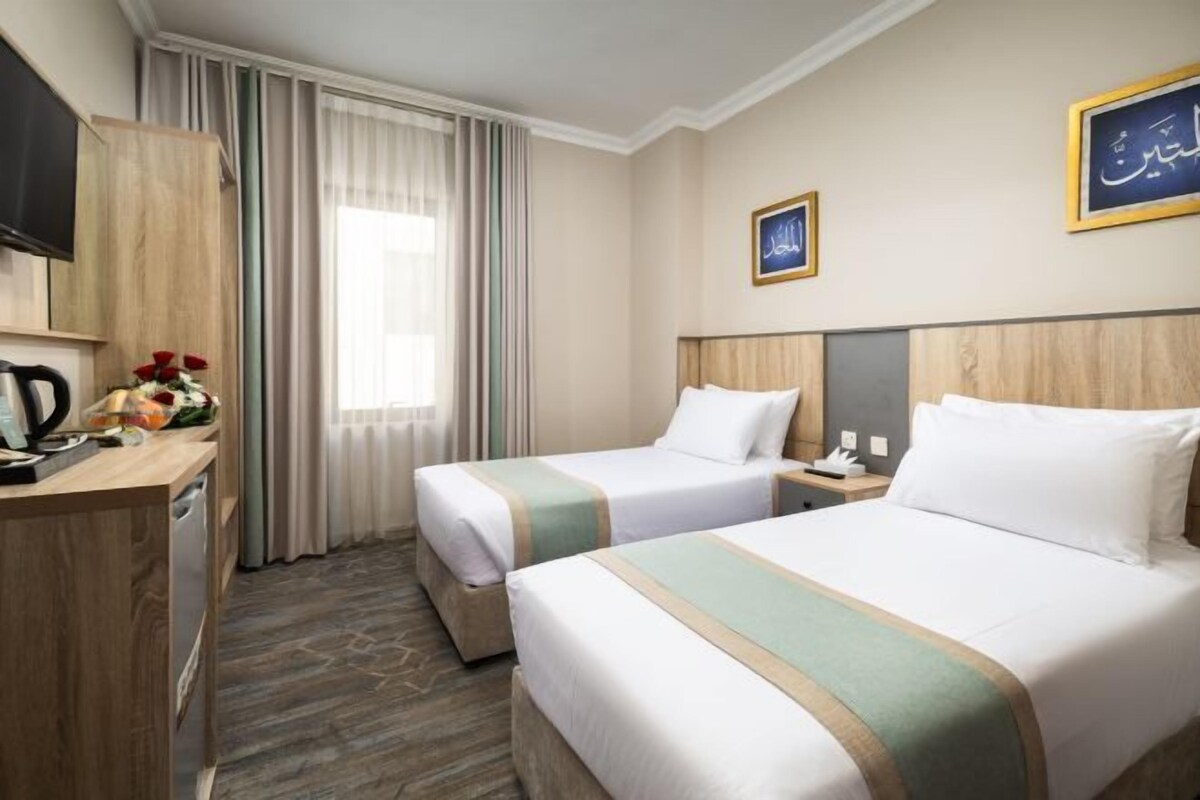 A hotel room with two beds, a desk with a coffee maker, a TV, and a window with curtains.