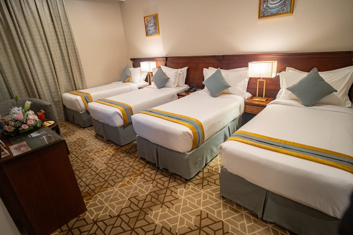 Ein Hotelzimmer mit drei Einzelbetten, einem Schreibtisch und einem Stuhl mit Blumenarrangement.