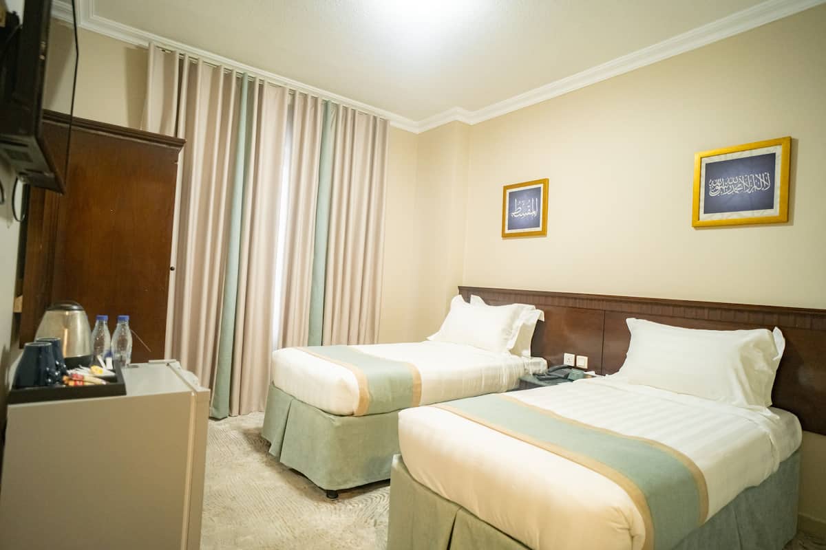Ein Hotelzimmer mit zwei Betten, einem Schreibtisch mit Lampe und einer Minibar.