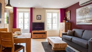 Una sala de estar amoblada con un sofá, una mesa de centro, un televisor sobre un mueble bajo y una mesa de comedor con sillas.