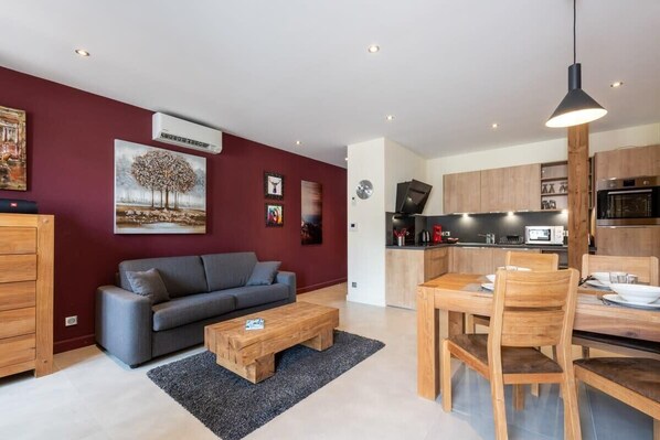 Un salon moderne avec un canapé gris, une table basse en bois et un coin repas comprenant une table et des chaises en bois.