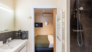 Un baño moderno con un lavamanos grande, ducha y una cama visible a través de una puerta abierta.