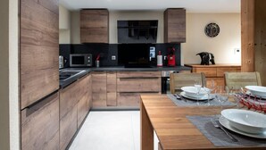 A modern kitchen with wooden cabinets, a black countertop, and a dining area with a wooden table and chairs. - APPALACHES, Annecy Rent Lodge (Annecy)