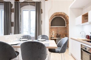 A modern kitchen with a brick oven, white cabinets, and a dining area with grey upholstered chairs.