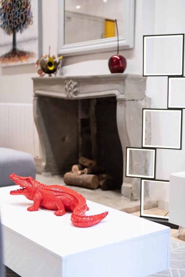 A room with a white fireplace, a red sculpture on a white table, and a mirror on the wall.