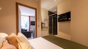 A hotel room with a bed, a shower area, and a television mounted on the wall. - CAUCASE, Annecy Rent Lodge (Annecy)