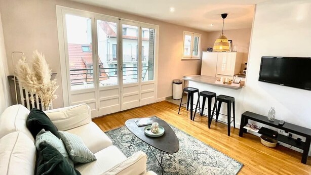 A modern living room with a sofa, coffee table, and a kitchen area with stools. - COSY HOME, Annecy Rent Lodge (Annecy)