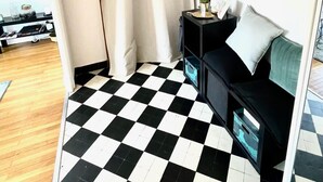 A room with a black and white checkered floor, a black sofa with a round mirror, a small table with a cactus, and a window with beige curtains. - COSY HOME, Annecy Rent Lodge (Annecy)