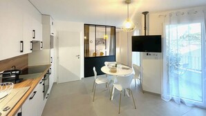 A modern kitchen with white cabinets, a wooden countertop, and a dining area with white chairs and a round table. - Le Quartz Tresum, in a modern residence near the lake, garage included (Annecy)