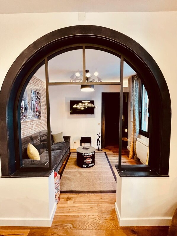 A modern living room with a black-framed archway, a grey sofa, a coffee table, and a TV mounted on the wall.