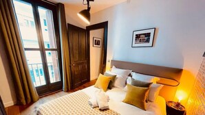 Habitación de hotel con cama, mesita de noche, lámpara, un cuadro en la pared y una ventana con cortinas.