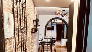 Un pasillo con pared de ladrillo, suelo de madera, una puerta negra y una zona de comedor con mesa y sillas.