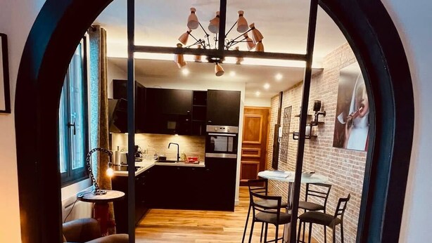 Una cocina moderna con una isla central, un área de comedor con sillas y un amplio ventanal de arco.