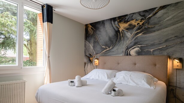 A neatly made bed with white linens and towels, a marble-patterned wall, and a window with curtains. - Les Pommaries - Calm T2 near the Lake (Annecy)