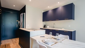 A modern kitchen with dark blue cabinets, a white countertop, and a dining area set for four. - Les Pommaries - Calm T2 near the Lake (Annecy)