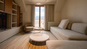 Una habitación de hotel moderna con sofá, sillón, mesa redonda de centro, televisión y estanterías empotradas.