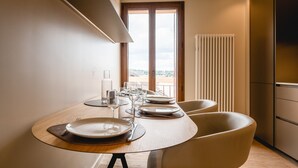 Un comedor moderno con una mesa redonda para dos personas, vistas al exterior a través de un gran ventanal y un horno empotrado en la cocina.