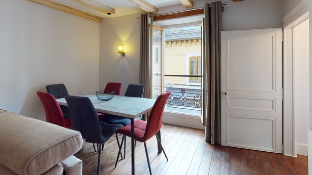 Een eetgedeelte met een houten tafel en stoelen, een wandlamp en uitzicht door een raam.