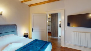 Een slaapkamer met een bed, een nachtkastje, een tv aan de muur en een houten plafond.