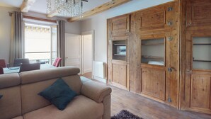 Een woonkamer met een beige bank, houten kasten en een kroonluchter.
