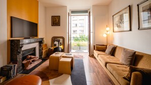 A living room with a fireplace, a sofa, a television, and a view of the outside balcony. - Le Cosy d'Aléry - Charming 3 room apartment near downtown (Annecy)