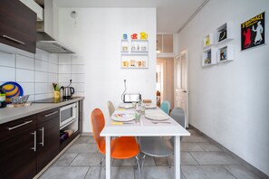 Una cocina moderna con armarios blancos, una mesa de comedor preparada para cuatro personas y un estante en la pared con utensilios de cocina.