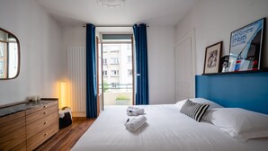 A hotel room with a bed, a dresser, a lamp, and a view of the outside. - Le Cosy d'Aléry - Charming 3 room apartment near downtown (Annecy)