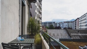 A balcony with a table and chairs, a potted plant, and a view of surrounding buildings and mountains. - Le Cosy d'Aléry - Charming 3 room apartment near downtown (Annecy)
