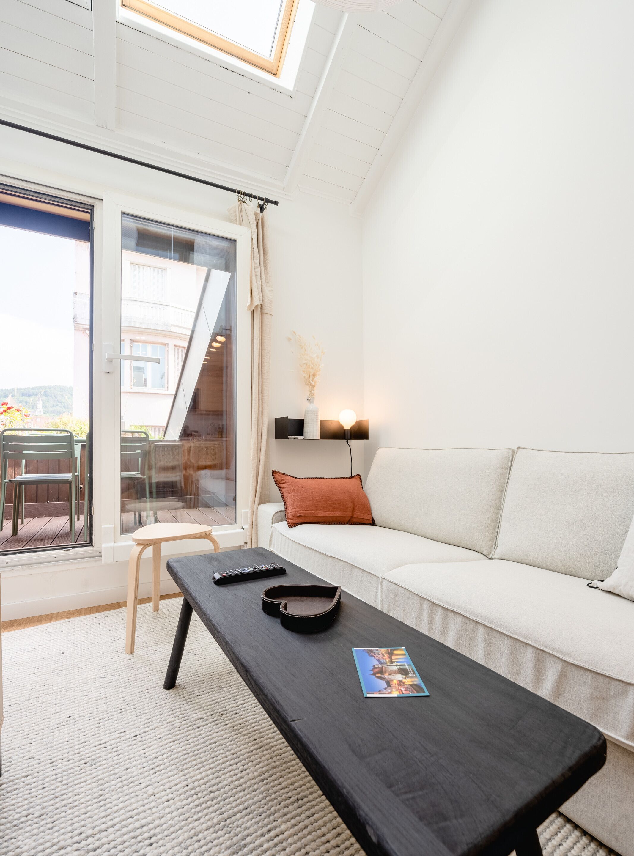 A modern living room with a sofa, a coffee table, and a view of the outdoors through a glass door.