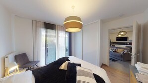 A modern hotel room with a large bed, a chair, a desk, and a view of the living area. - Le Confort Annecy (terrasse & parking privé) (Annecy)