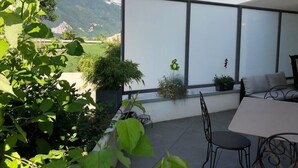 A modern outdoor patio with a table and chairs, surrounded by potted plants and a view of mountains. - Le Confort Annecy (terrasse & parking privé) (Annecy)