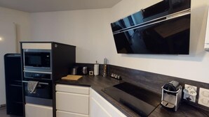 A compact kitchen with a microwave, oven, and a coffee machine. A flat-screen TV is mounted on the wall above the counter. - Le Confort Annecy (terrasse & parking privé) (Annecy)