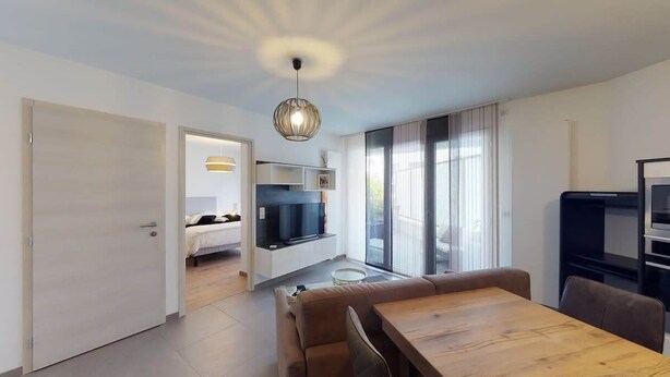 A modern living room with a wooden dining table, a sofa, and a TV in the background. - Le Confort Annecy (terrasse & parking privé) (Annecy)