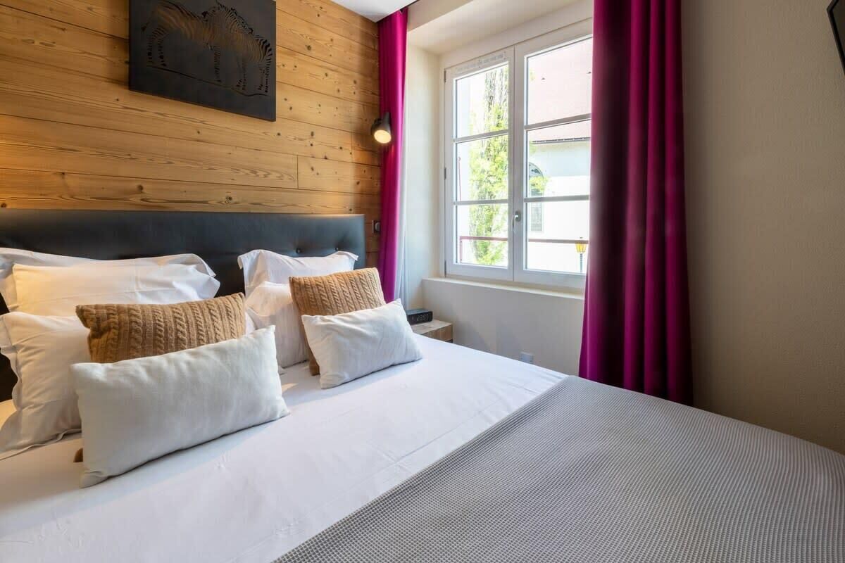 A hotel room with a wooden headboard, a large bed with white bedding, and a window with curtains.