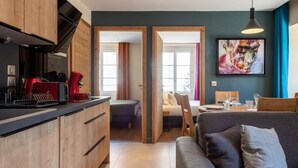 A modern kitchen with wooden cabinets and a dining area with a gray sofa and a table set for two. - OURAL, Annecy Rent Lodge (Annecy)