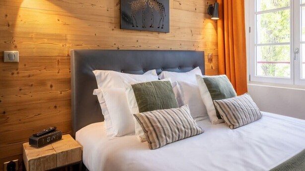 A neatly made bed with white and striped pillows, a wooden headboard, and a giraffe artwork on the wall. - OURAL, Annecy Rent Lodge (Annecy)