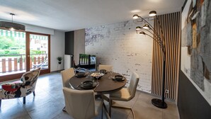 Un coin repas avec une table ronde dressée pour quatre personnes, entourée de chaises. Une grande fenêtre offre une vue sur l’extérieur.