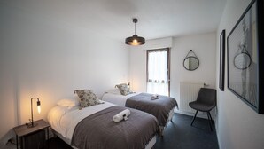 Une chambre moderne avec deux lits, une table de chevet avec une lampe, une chaise et une fenêtre avec des rideaux.